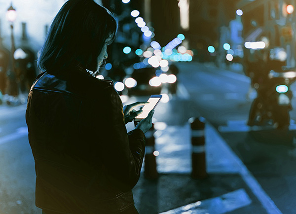 Woman in a leather jacket using a phone outside at night.